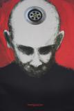Plakat przedstawiający popiersie łysego mężczyzny o szarej cerze na czerwonym tle, ubranego w czarną koszulkę, spoglądającego w dół. Na szczycie jego głowy widać dziurę od zlewu. Na dole zdjęcia napis "MANIPULATION". 